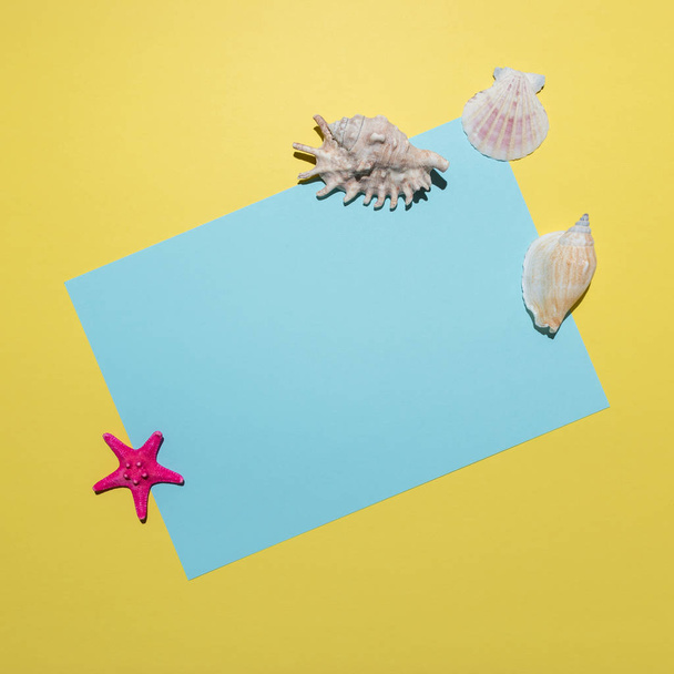 Kreative Komposition mit Muscheln und blauer Papierkarte auf leuchtend gelbem Hintergrund. Minimalkonzept Sommer. - Foto, Bild