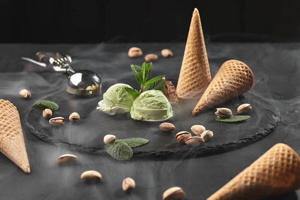 Изысканный шоколад и фисташковое мороженое подаются на каменной доске на черном фоне
. - Фото, изображение
