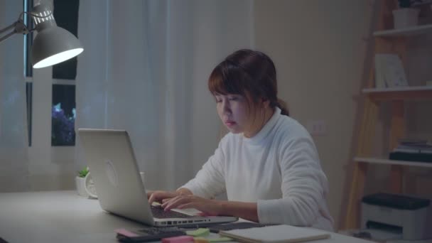 Fiatal ázsiai nő dolgozik késő használ laptop-ra iskolapad nappaliban otthon. Ázsia teendő nő írás jegyzetfüzet dokumentum Pénzügy és számológép-ban éjszaka-on haza hivatal. Hányinger és fáradt. - Felvétel, videó