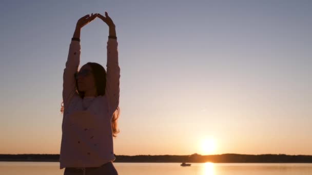 junge Frau genießt Sonnenuntergang zur goldenen Stunde am Flussstrand im Frühling in weißer Hose, Jogginghose und Jacke - kaukasisches weißes Mädchen ist eine glückliche Reisende - Filmmaterial, Video