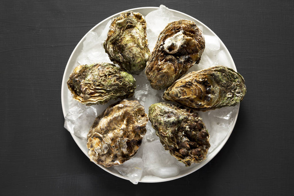 Top view, fresh oysters on ice on gray plate over black backgrou - Foto, Imagen