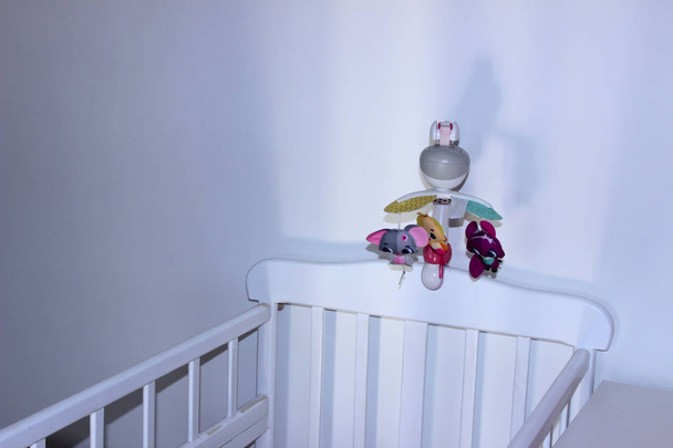 Kasvatettu kuva lastenhuoneesta. Valkoinen vauvan sänky vastasyntyneelle yli Valkoisen muurin tausta. Valkoinen sisustus vauvan puomi
. - Valokuva, kuva