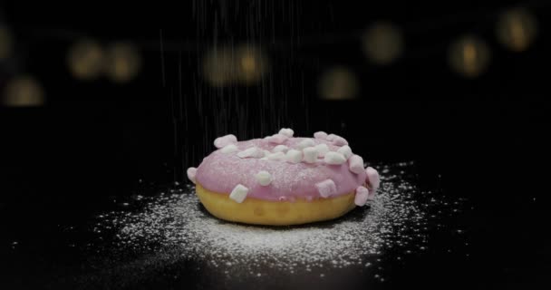 leckerer frischer Donut liegt auf schwarzer Oberfläche und wird mit Puderzuckerpulver bestreut - Filmmaterial, Video