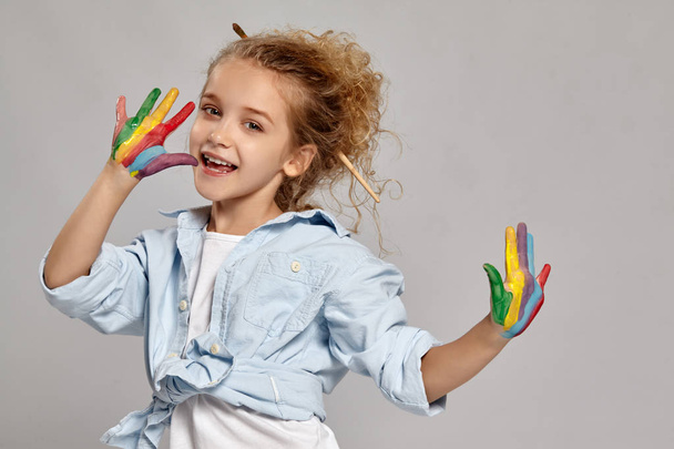 Beautiful little girl with a painted hands is posing on a gray background. - Foto, imagen