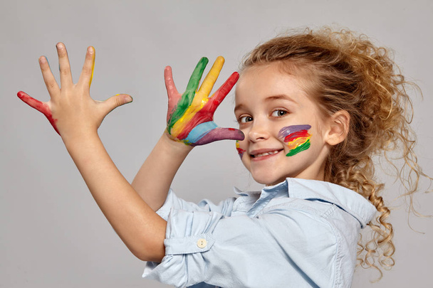 Beautiful little girl with a painted hands and cheeks is posing on a gray background. - Foto, Bild