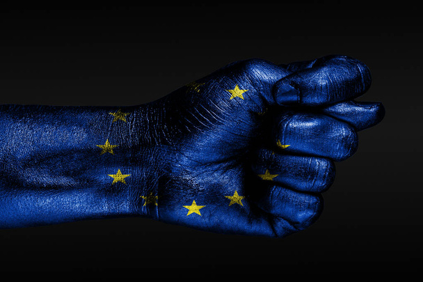 Une main avec un drapeau peint de l'UE montre une figue, un signe d'agression, un désaccord, un différend sur un fond sombre
. - Photo, image