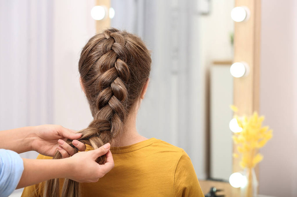 Professional coiffeuse braiding client's hair in salon - 写真・画像