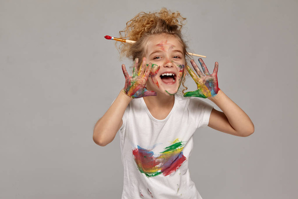 Hermosa niña con las manos y las mejillas pintadas posando sobre un fondo gris
. - Foto, Imagen