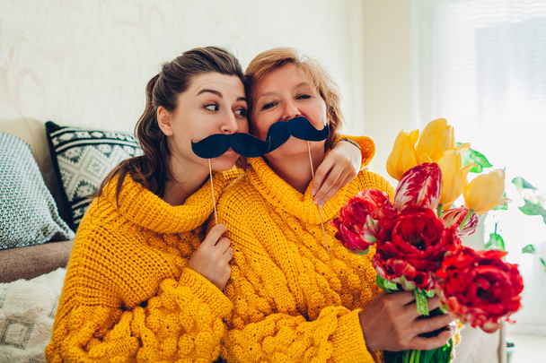 Senior moeder en haar volwassen dochter nemen selfie met bloemen met behulp van Photo Booth Props thuis. Mother's Day concept. - Foto, afbeelding