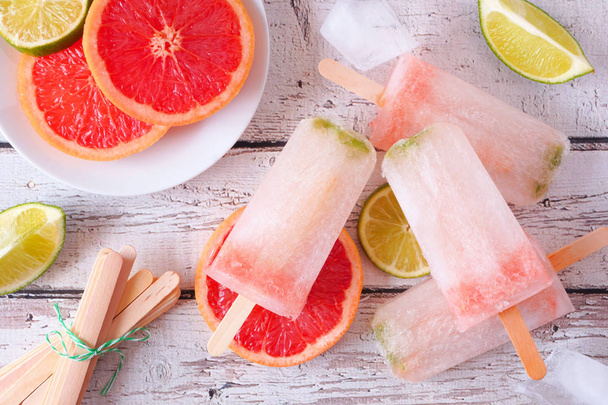 Sparkling lime and grapefruit popsicles, top view table scene against a white wood background - Foto, afbeelding