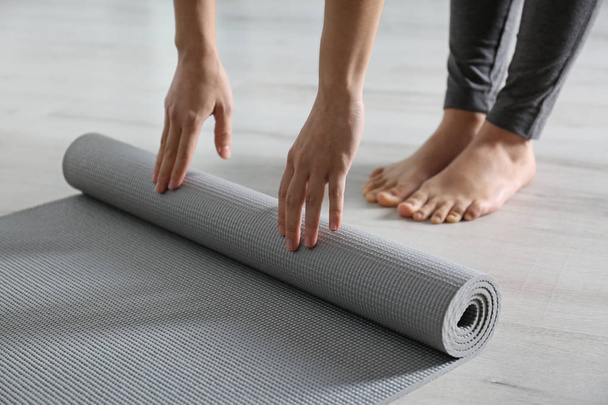 Woman rolling yoga mat on floor indoors, closeup - 写真・画像