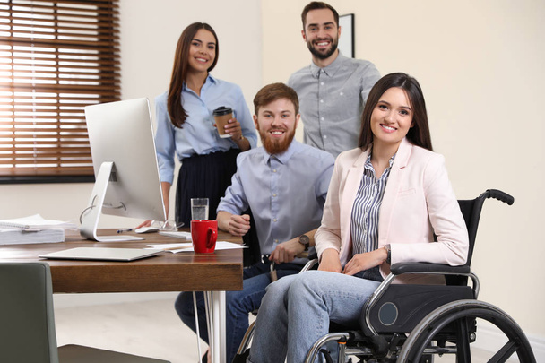 Young woman in wheelchair with colleagues at workplace - Fotografie, Obrázek