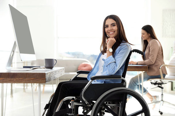 Young woman in wheelchair using computer at workplace - Photo, Image
