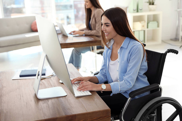 Young woman in wheelchair using computer at workplace - Foto, Imagen