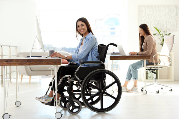 Young woman in wheelchair using computer at workplace - Valokuva, kuva