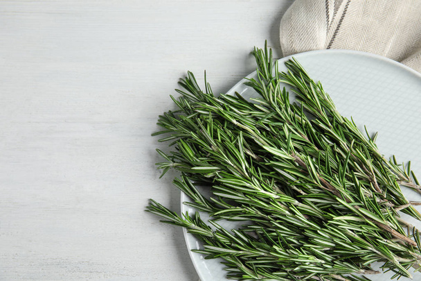 Plate with fresh rosemary twigs on wooden table, top view. Space for text - 写真・画像