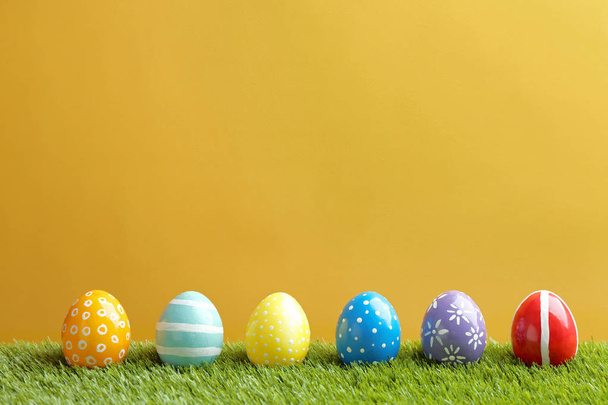 Painted Easter eggs on green grass against color background, space for text - Photo, image