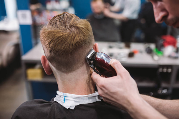 lähikuva miehestä parturissa trendikkäässä kampauksessa. Mies kampaaja palvelee asiakasta, joten hiustenleikkaus koneella ja kammalla
 - Valokuva, kuva