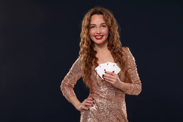 Mooie jonge emotionele vrouw in cocktail jurk toont haar kaarten aan de tegenstander, vier van azen, beste hand. Blcak achtergrond, Studio schot - Foto, afbeelding