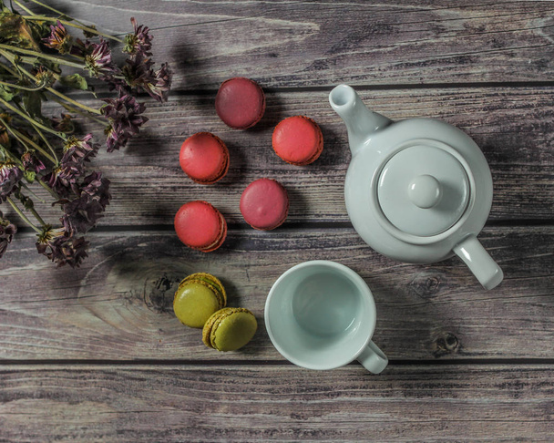 White teapot, cup, bouquet of field flowers and colorful macaroons on the wooden table. - Fotografie, Obrázek