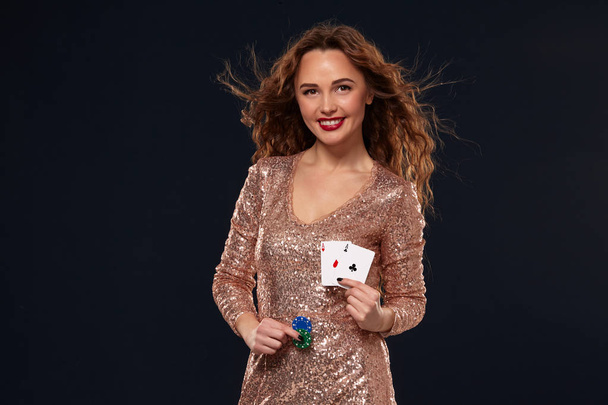 Bruin harige aantrekkelijke Kaukasische jonge vrouw in gouden cocktail jurk in Casino houdt paar azen en chips in haar handen - Foto, afbeelding