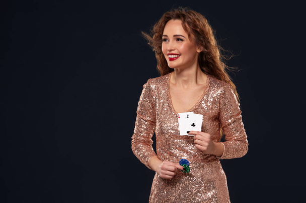 Bruin harige aantrekkelijke Kaukasische jonge vrouw in gouden cocktail jurk in Casino houdt paar azen en chips in haar handen - Foto, afbeelding