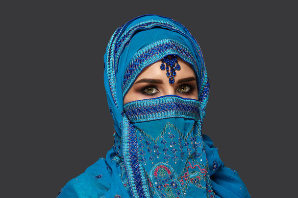 Studio girato di una giovane bella donna che indossa l'hijab blu decorato con paillettes e gioielli. Stile arabo
. - Foto, immagini
