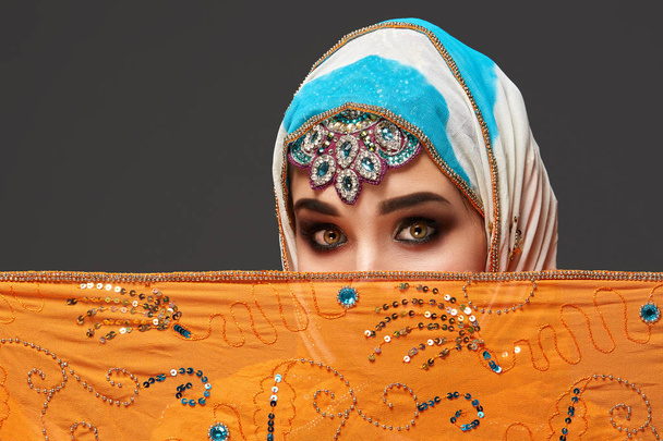 Studio shot of a chrming female wearing the colorful hijab decorated with sequins and jewelry. Arabic style. - Photo, Image