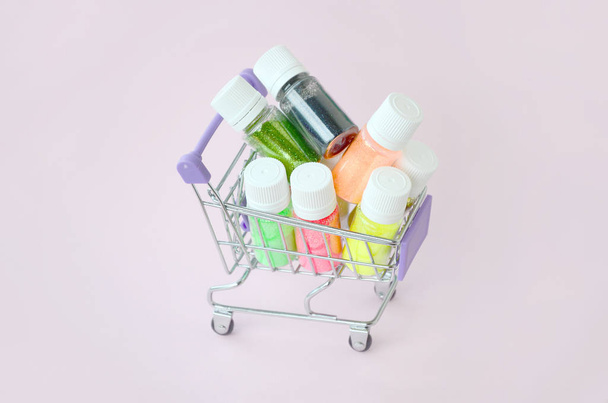 El carrito de compras está lleno de muchos frascos redondos con destellos brillantes multicolores para esmalte de uñas. Lentejuelas espumosas
 - Foto, imagen