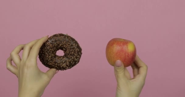 Τα χέρια κρατούν ντόνατ και μήλο. Επιλογή ντόνατ εναντίον μήλου. Υγιεινό ή πρόχειρο φαγητό - Πλάνα, βίντεο