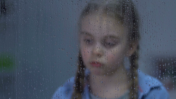 Αναστατωμένος κορίτσι κοιτάζοντας στο παράθυρο στη βροχή, υποφέρουν μοναξιά, περιμένοντας τους γονείς - Πλάνα, βίντεο