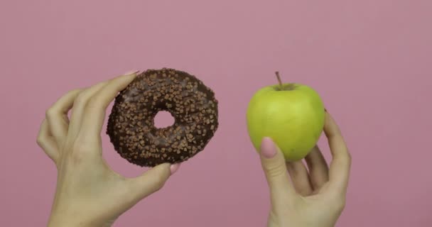 Ręce trzyma pączek i jabłko. Wybór pączka przeciwko jabłko. Zdrowe lub śmieciowe jedzenie - Materiał filmowy, wideo
