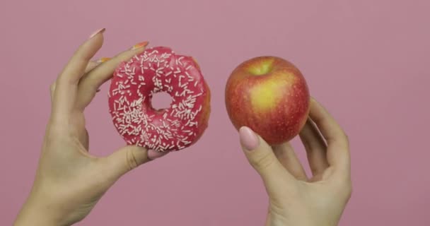 Τα χέρια κρατούν ντόνατ και μήλο. Επιλογή ντόνατ εναντίον μήλου. Υγιεινό ή πρόχειρο φαγητό - Πλάνα, βίντεο