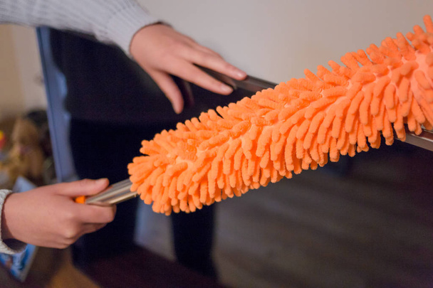 Young woman, wife using orange duster to collect dust from the tv - Photo, image