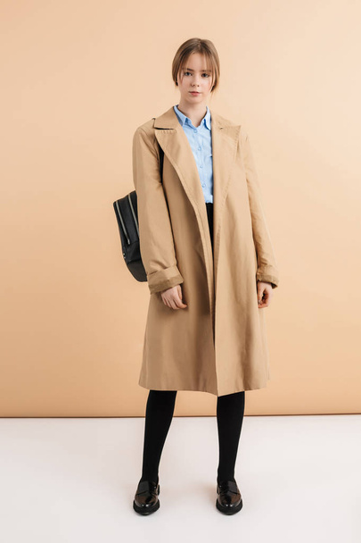 Menina bonita nova em casaco de trincheira e camisa com backpac preto
 - Foto, Imagem