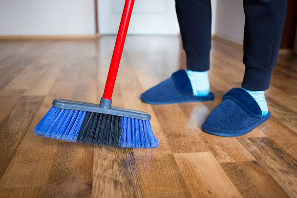 Woman, wife in blue slippers using indoor blue broom for hardwood floor cleaning - Photo, image