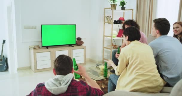 Excited group of multi ethnic friends watching a football match in the tv with a green screen they happy support and celebrating the first goal of their team , standing up yelling and get the hands up - Metraje, vídeo