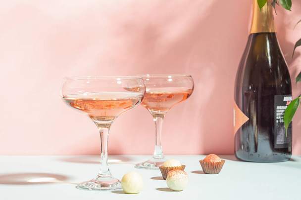 Champagne or wine in elegant glasses, a box of chocolates pink background of bright light. Copy space. Selective focus. - Фото, зображення
