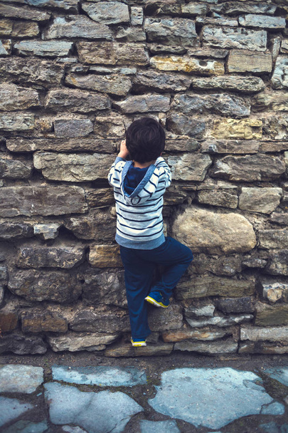 Мальчик перелез через каменный забор
. - Фото, изображение