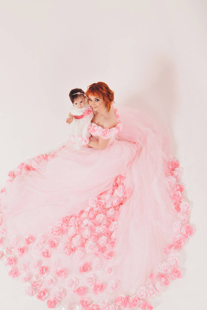 the child in the arms of his mother in a pink dress of flowers. A woman with a child in her arms on a white background, isolated - Photo, Image