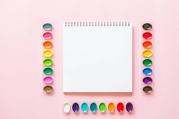 Diseño plano creativo de paletas de acuarela y cuaderno. Lugar de trabajo del artista sobre un fondo pastel rosa
. - Foto, imagen