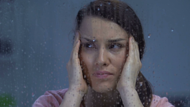 Migreni olan bir kadın, yağmurlu pencerenin yakınındaki tapınakları ovuyor, hava hassasiyeti var. - Video, Çekim