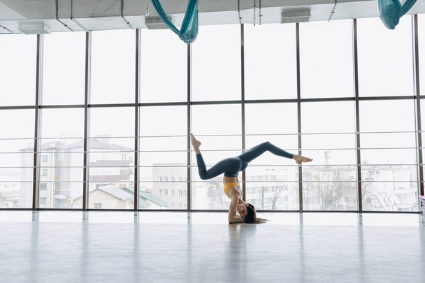 junges attraktives Mädchen macht Fitnessübungen mit Yoga auf dem Boden vor dem Hintergrund von Panoramafenstern - Foto, Bild