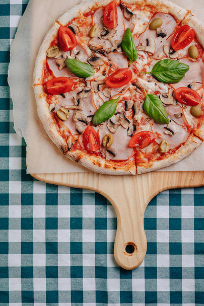 Napolilainen pizza sienillä, juustolla, arugulalla, basilikalla, tomaateilla, jotka on siroteltu juustolla puulaudalle pöytäliinalla sellissä, jossa on paikka tekstille.
 - Valokuva, kuva