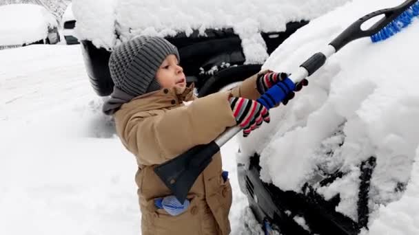 4K wideo 3-letniego chłopca malucha pomaga czyszczenia samochodu pokryte śniegiem po burzy śnieżnej - Materiał filmowy, wideo
