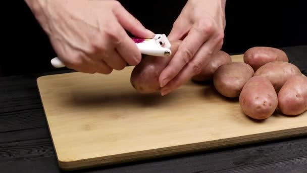 Las manos femeninas del chef pelan patatas para freír o guisar. Parte del proceso de cocción en la receta casera
. - Imágenes, Vídeo