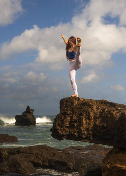 young attractive and concentrated woman practicing acroyoga balance exercise and yoga flexibility and meditation at beautiful beach rock cliff in healthy lifestyle - Valokuva, kuva