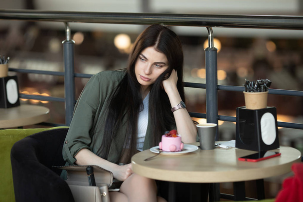 Portret szczęśliwej kobiety jedzącej kawałek ciasta i pijącej kawę siedząc przy stole w kawiarni - Zdjęcie, obraz