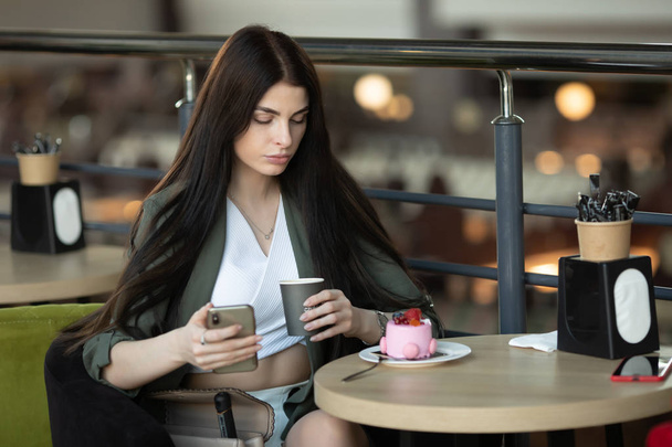 Ritratto di una donna felice che mangia un pezzo di torta e beve caffè mentre si siede a tavola in un caffè al chiuso - Foto, immagini