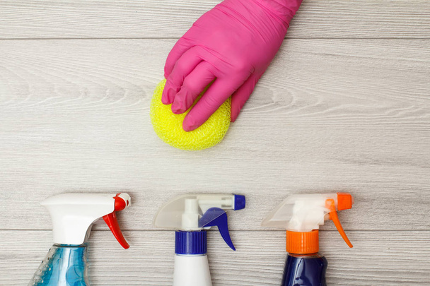 Hand in rubber glove holding sponge with bottles of detergent. - Foto, imagen